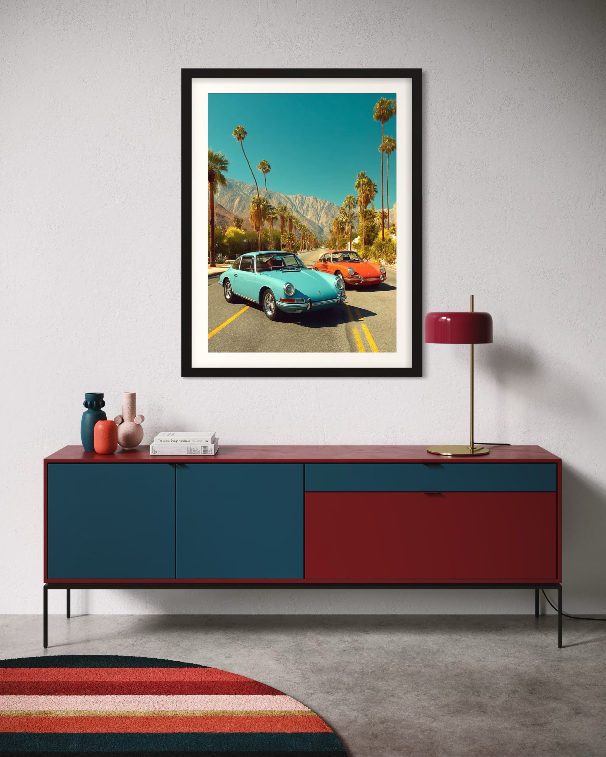 Framed artwork of vintage 9111T Porsche cars on a wall above a red and blue cabinet.
