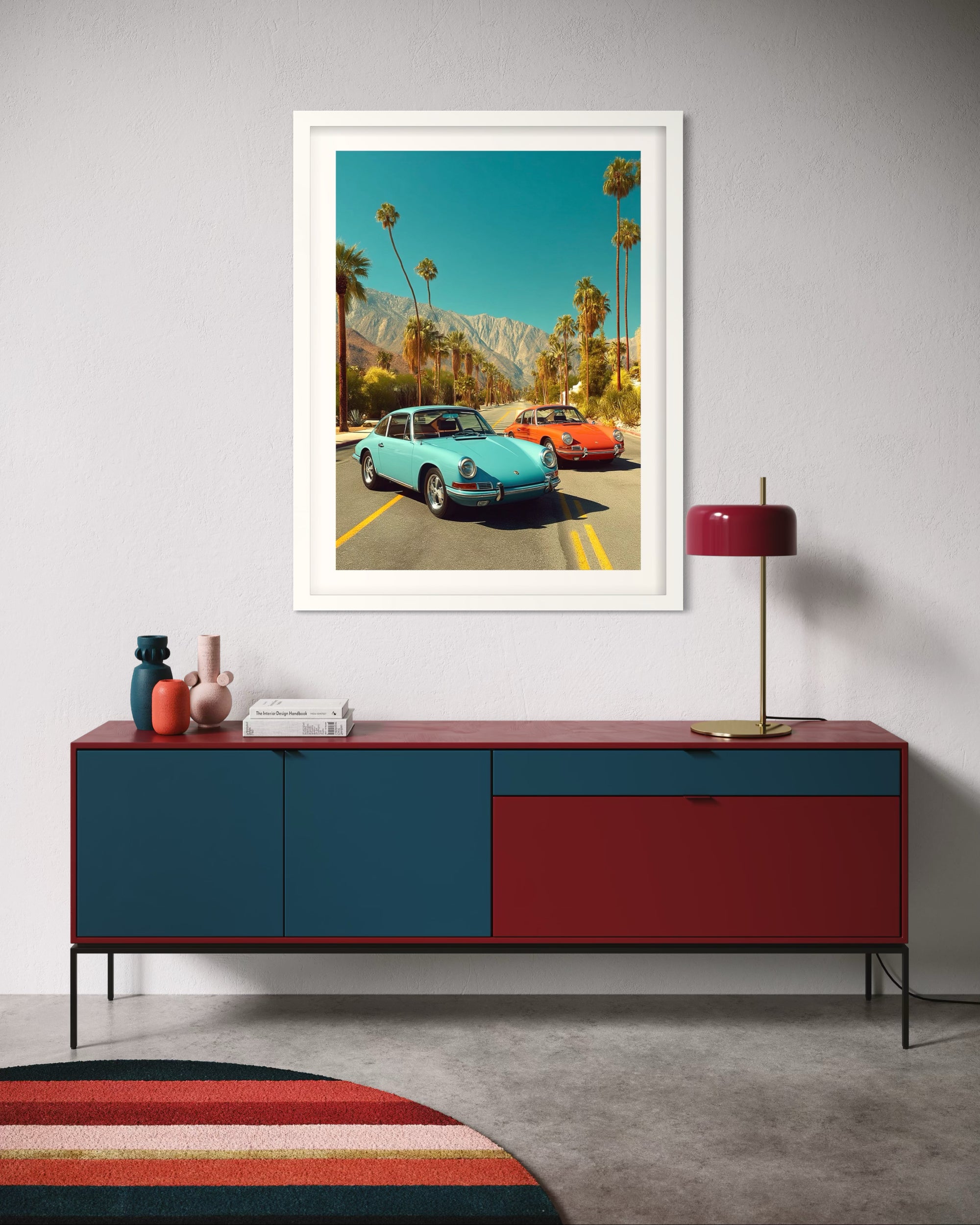 Framed artwork of vintage 9111T Porsche cars on a wall above a red and blue sideboard.