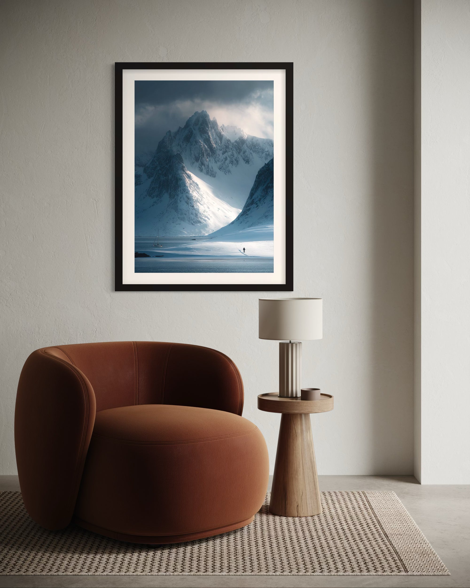 Framed snowy mountain landscape print on a wall above a brown armchair in a room.