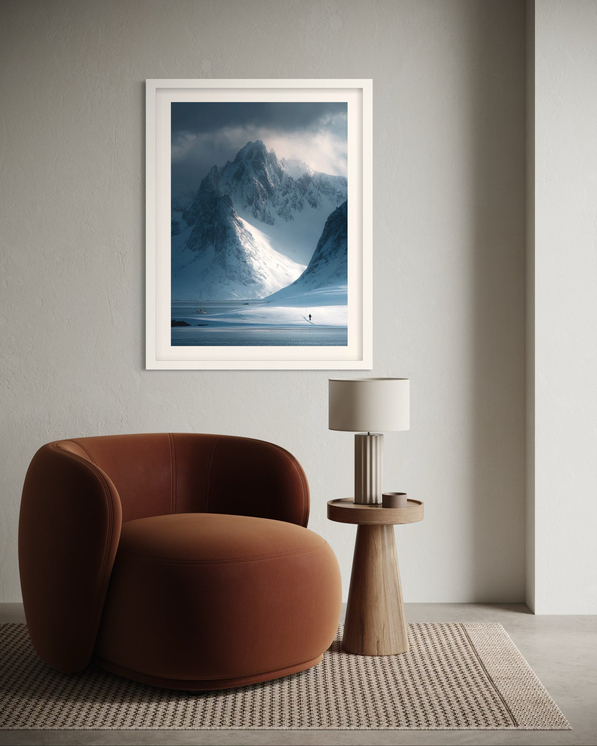 Framed snowy mountain landscape print above a brown armchair in a room.